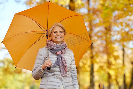 保险伞摄影照片_老年，天气和季节概念—愉快的老年妇女的肖像与伞在秋天公园。愉快的老年妇女与伞在秋天公园