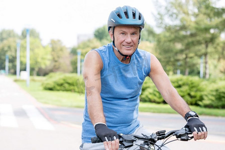 戴头盔摄影照片_公园骑自行车时戴头盔的老人肖像