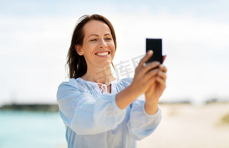 暑假和休闲概念—愉快的微笑妇女采取自拍在海滩。快乐的微笑妇女采取自拍在夏季海滩