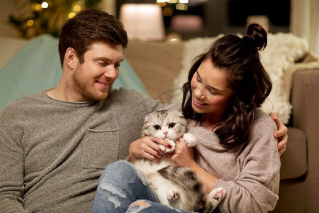 天猫天猫圣诞摄影照片_宠物，hygge和人的概念—快乐的夫妇与猫在家里。快乐的夫妇与猫在家里