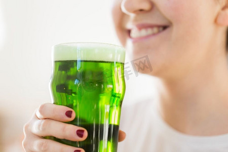 酒精和圣帕特里克节的概念-玻璃杯中拿着绿啤酒的女人的特写。玻璃杯中拿着绿啤酒的女人的特写