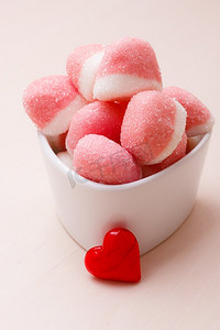 红状摄影照片_甜食糖果。粉红色果冻或棉花糖与糖在白色碗木桌上装饰有红心爱的象征