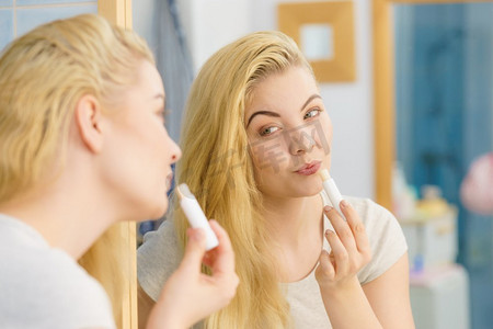 金发女人在浴室里放应用润唇膏保湿香脂，照顾她的嘴唇皮肤。妇女在浴室应用唇膏
