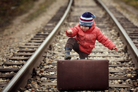 在铁路上提着行李箱的小旅行者