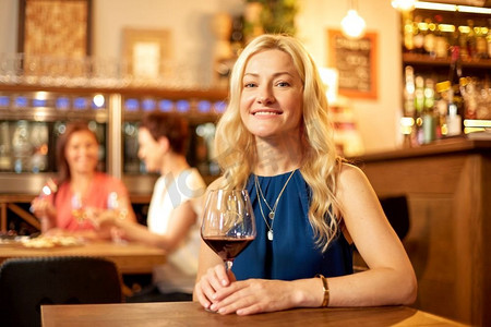 人，酒精和生活方式的概念—快乐的女人喝红葡萄酒在餐厅或酒吧。在酒吧或餐馆喝红酒的快乐女人