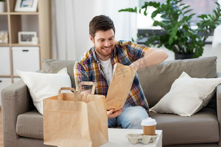 消费，吃和人的概念—微笑的男子打开外卖食品在家里。微笑的男人在家里打开外卖食品