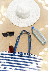 水袋气球摄影照片_度假，旅行和夏季概念—沙滩袋，防晒霜，太阳镜和帽子在沙滩上。沙滩袋，防晒霜，太阳镜和帽子在沙滩上