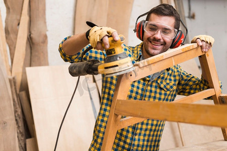 一个熟练的木匠用动力砂光机作为工具打磨家具
