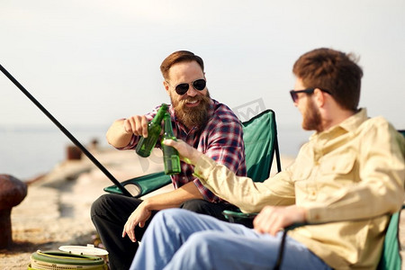 夏日啤酒饮料摄影照片_消闲与人的概念—夏日，朋友在码头钓鱼、喝啤酒。快乐的朋友钓鱼和喝啤酒在码头
