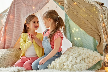 童年，hygge和友谊的概念—小女孩在孩子的帐篷或帐篷在家里谈话。小女孩说话在孩子帐篷在家里
