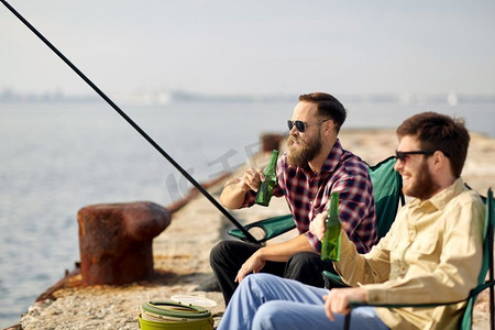 休闲与人的概念—快乐的朋友在码头钓鱼和喝啤酒。快乐的朋友钓鱼和喝啤酒在码头