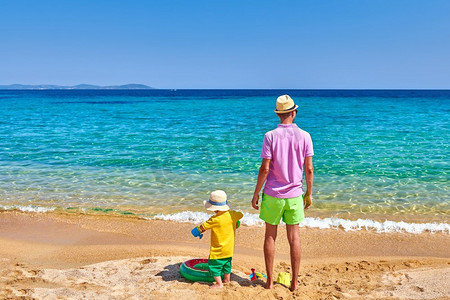 两岁的小男孩和父亲在海滩上。充气戒指和沙滩玩具。暑假家庭度假。希腊，西托尼亚。 