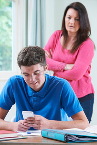 母亲看起来不赞成十几岁的儿子在学习时使用手机