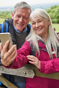 微笑的老年夫妇徒步在农村站在门口和采取自拍手机                                   