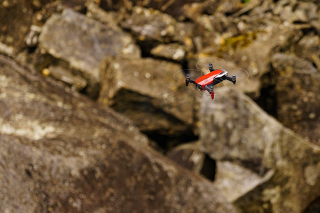 红色紧凑型无人机在岩石上对自然飞行，拍照和录像。无人机飞越岩石