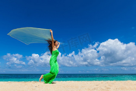 年轻漂亮的女人手持布料在海滩上奔跑。穿着礼服的女子在海滩上奔跑