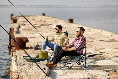 喝啤酒摄影照片_休闲与人的概念—快乐的朋友在码头钓鱼和喝啤酒。快乐的朋友钓鱼和喝啤酒在码头