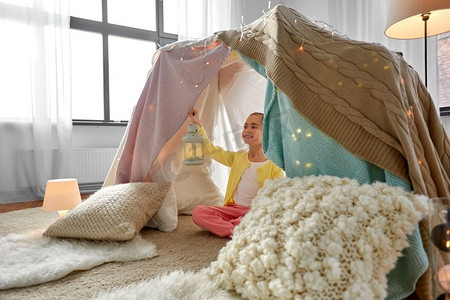 童年和hygge概念—有灯笼的快乐的小女孩在孩子帐篷或帐篷在家里小女孩与灯笼在孩子们帐篷在家里