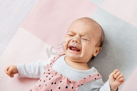 婴儿、母亲和人的概念-哭闹的小女孩躺在针织毯子上。哭闹的女婴躺在针织毯子上