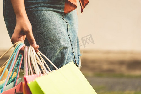 妇女的特写镜头持有彩色纸购物袋在街道。夏季促销和黑色星期五购物概念。复古色调电影封面大小的照片。