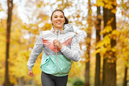 健身，运动，人和健康的生活方式概念—年轻女子跑步在秋天公园。在秋天公园跑步的年轻女子