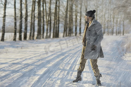 穿着大衣/冬季风格的时髦男子，在冬季风景的背景下行走，下雪的天气，保暖的衣服