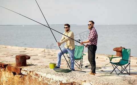 趣味钓鱼摄影照片_休闲与人的概念—在海上码头与钓竿快乐的朋友。快乐的朋友与钓竿在码头