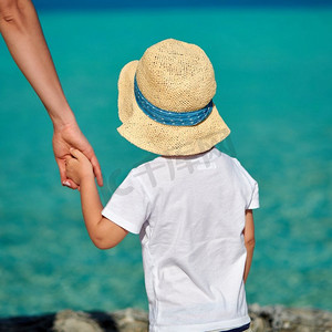 三岁的蹒跚学步的男孩在海滩上牵着妈妈的手。’暑假在马尔代夫度假。