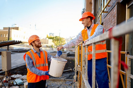建筑工人在工地上互相帮助。建筑工人将石膏桶送到同事那里。建筑工人在工地上互相帮助