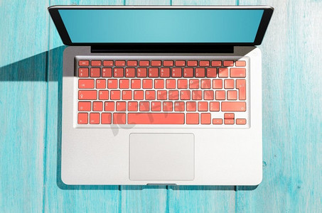 有生活珊瑚色键盘的膝上型计算机在木桌在晴天，从上面的看法。笔记本电脑在木桌上