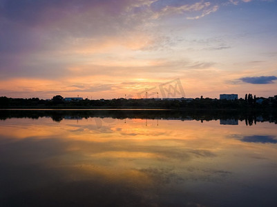 五颜六色的夕阳云对称地反射在湖面上。田园诗般的夏天晚上，自然景色附近的乡村池塘与平静的水。