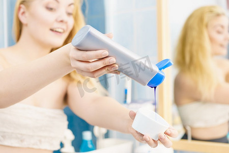 妇女倒紫色染发剂或洗发水到白色碗。卫生用品概念妇女倒紫色染发剂或洗发水