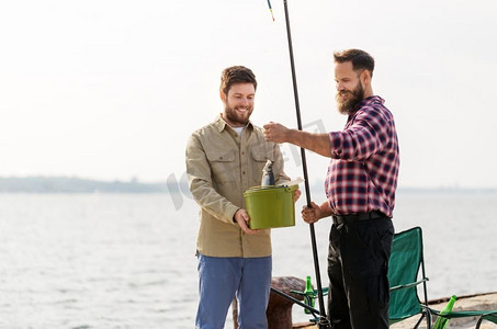 休闲和人的概念—快乐的男性朋友与鱼和钓竿在海上码头。男性朋友与鱼和钓竿在码头