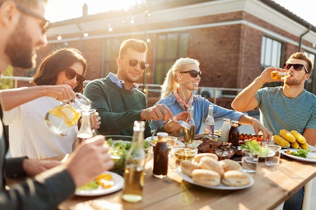休闲与人际概念—快乐的朋友在天台烧烤聚会上吃喝。朋友在屋顶吃晚餐或烧烤派对