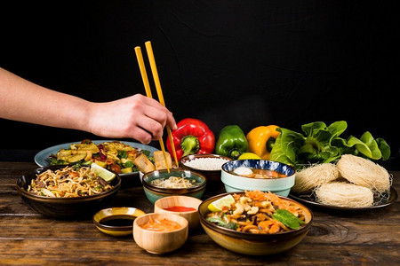 关闭人的手吃泰国食物与筷子桌子反对黑色背景