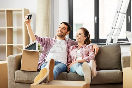 搬家、修缮、置业概念--微笑的夫妻在新家用智能手机自拍。情侣在新家用智能手机自拍
