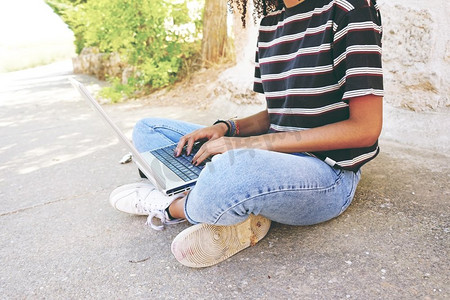 一个年轻的黑人妇女卷发，穿着牛仔裤和条纹t恤，坐在地上工作或做作业。