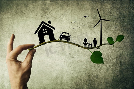 人类的手握着树枝。环境绿色能源理念。幸福的家庭、房子、汽车和风车的剪影