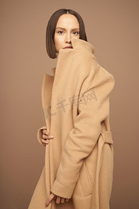 时尚工作室照片，年轻美丽的女士在米色背景下穿着米色外套。完全是米色。时尚装扮书。温暖的秋天。春暖花开