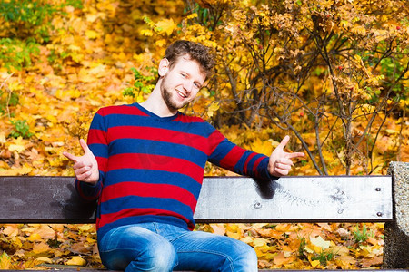 季节、幸福和人的观念。阳光明媚的秋天，一位留着胡须的年轻男子悠闲地坐在秋日公园的长凳上。公园里坐在长凳上的男人