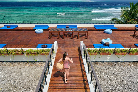 穿着红色条纹连体式泳衣的女子走在热带海滩露台甲板上。在马尔代夫度暑假。