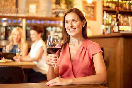 人，酒精和生活方式的概念—快乐的女人喝红葡萄酒在餐厅或酒吧。在酒吧或餐馆喝红酒的快乐女人