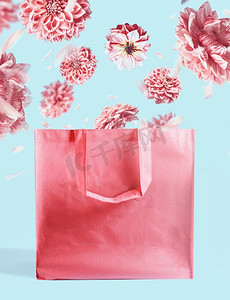 粉色购物袋，粉色蓝色墙壁背景，花朵飞扬。品牌推广的模拟。复制空间。创意夏日概念