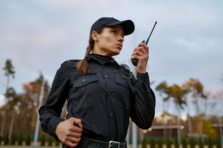 身穿制服的年轻女警察对着对讲机说着话。街道巡逻服务。巡逻女警对着对讲机讲话