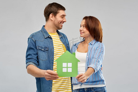 房子抵押摄影照片_房地产，家庭和生态概念—微笑的夫妇拿着绿色纸房子在灰色背景。微笑的夫妇抱着绿色的纸房子