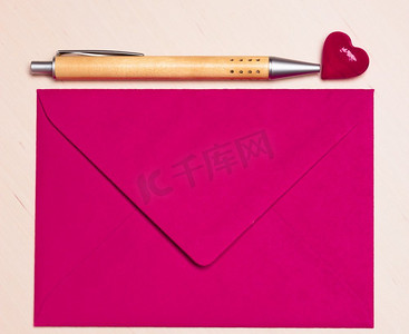 粉色的空白信封，木面上有小心形和钢笔。情人节贺卡，爱情或婚礼的问候概念。