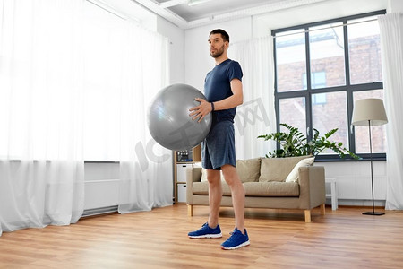 健身，运动和健康的生活方式概念—男子在家里用球锻炼。男子在家里用健身球锻炼