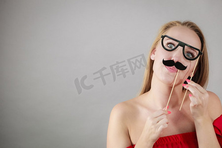 快乐的女人拿着假胡子玩得很开心。照片和嘉年华搞笑配饰概念..快乐的女人在棍子上举着假胡子