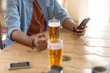 人和科技的概念--在酒吧或酒吧里，拿着智能手机喝啤酒、看短信的人。手持智能手机的男子在酒吧或酒吧喝啤酒