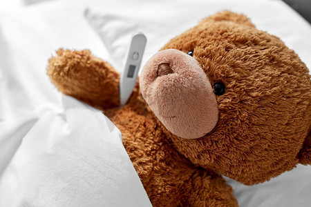 医学、保健和儿童概念-生病的泰迪熊玩具头，温度计躺在床上。生病的泰迪熊玩具头，床上有温度计